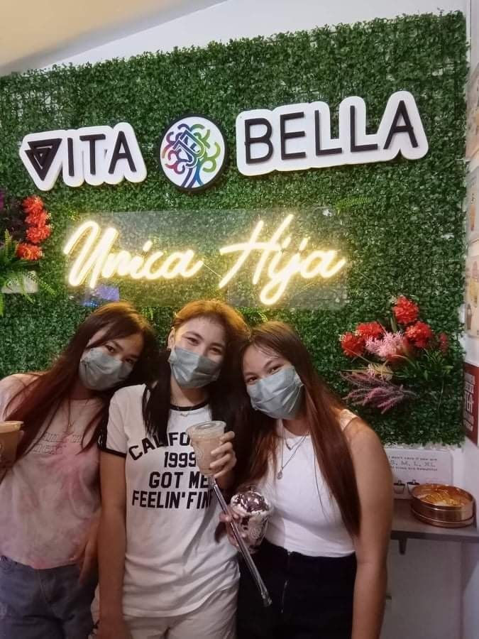 Customers with their drinks in front of a Vita Bella neon sign